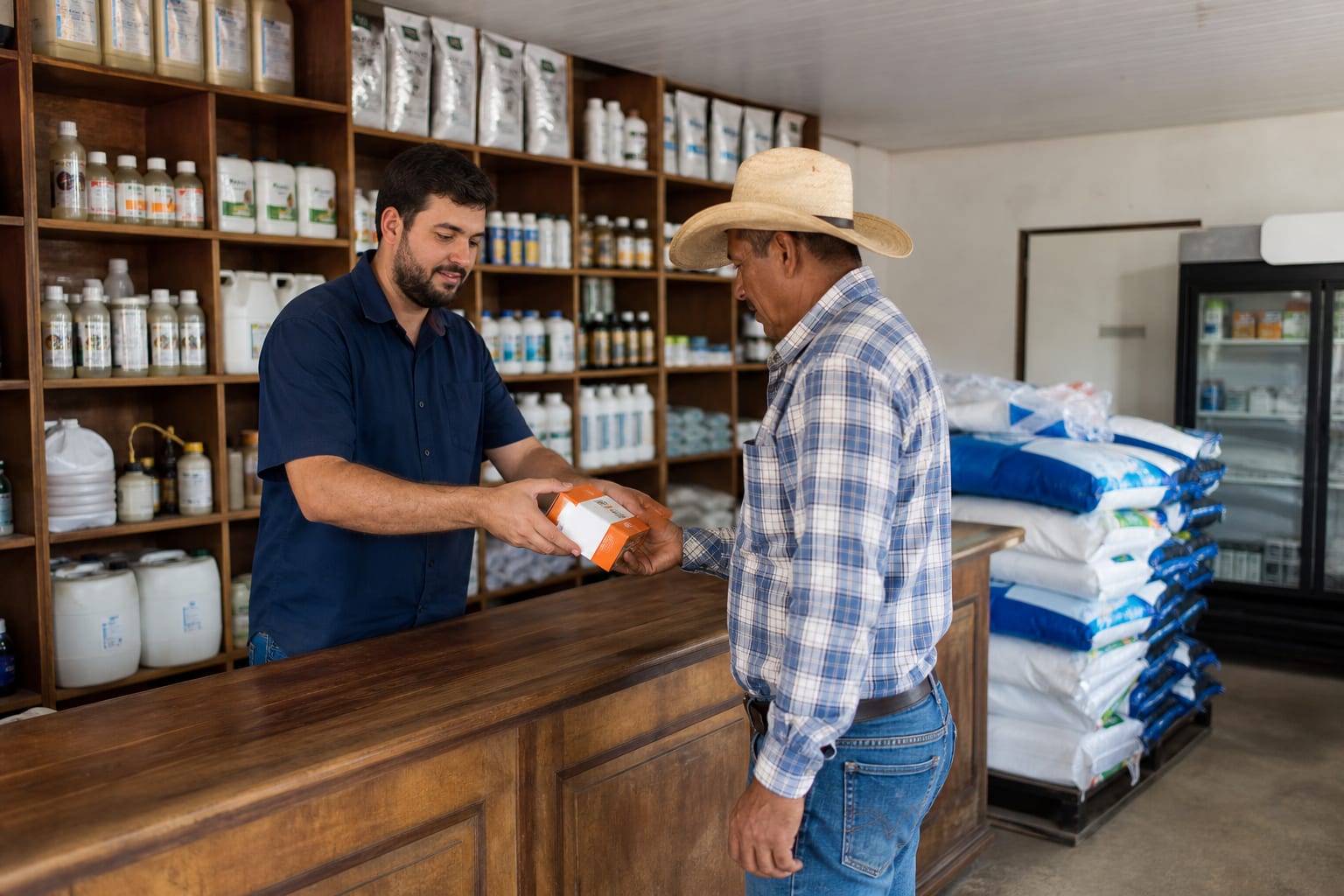 Atendente de casa agropecuária entrega caixa de medicamento veterinário a um produtor no balcão